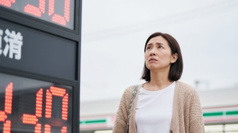 ガソリンスタンドで価格表示を確認しながら家計を考える30代日本人女性